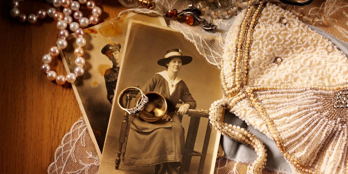 Old jewellery laid out across old brown photos of a man and woman. Two rings, a wedding and engagement rind sit atop of them